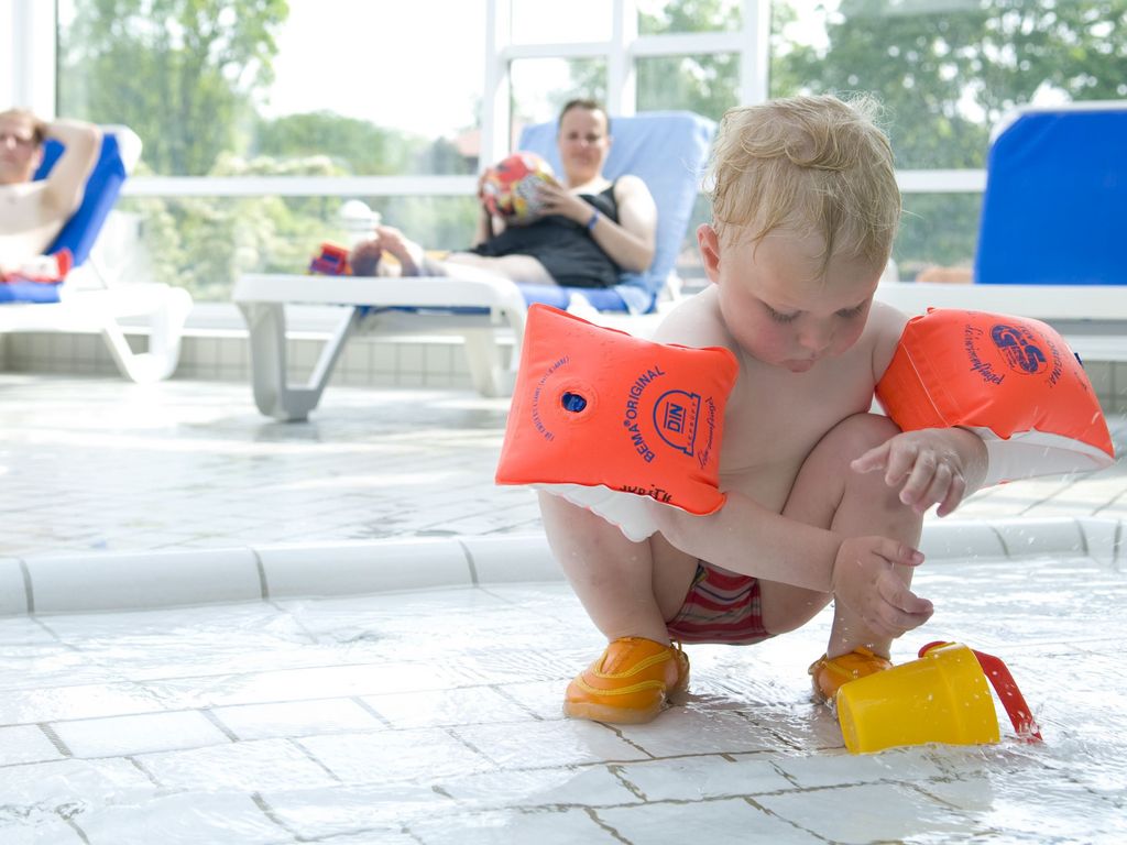 Kleinkindbereich · Kind mit Schwimmflügeln mit Liegen im Hintergrund