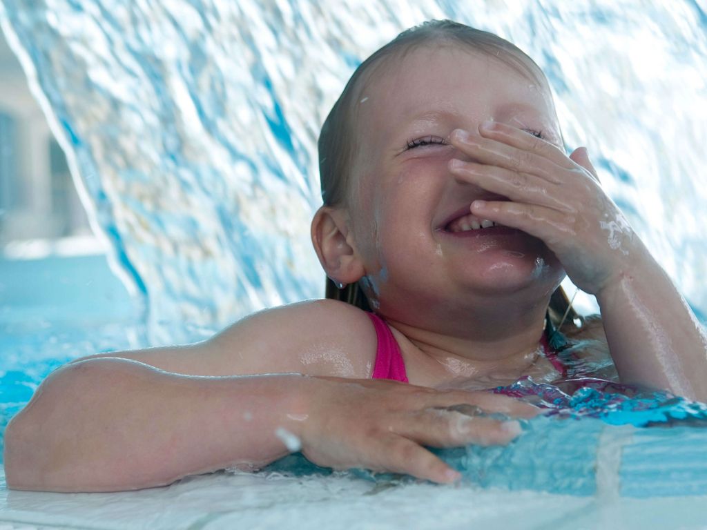 Spaßbecken · Kind unter Schwalldusche lachend